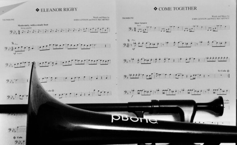 Sheet music for "Eleanor Rigby" and "Come Together" by The Beatles is overshadowed by the bell of a trombone resting on the stand.